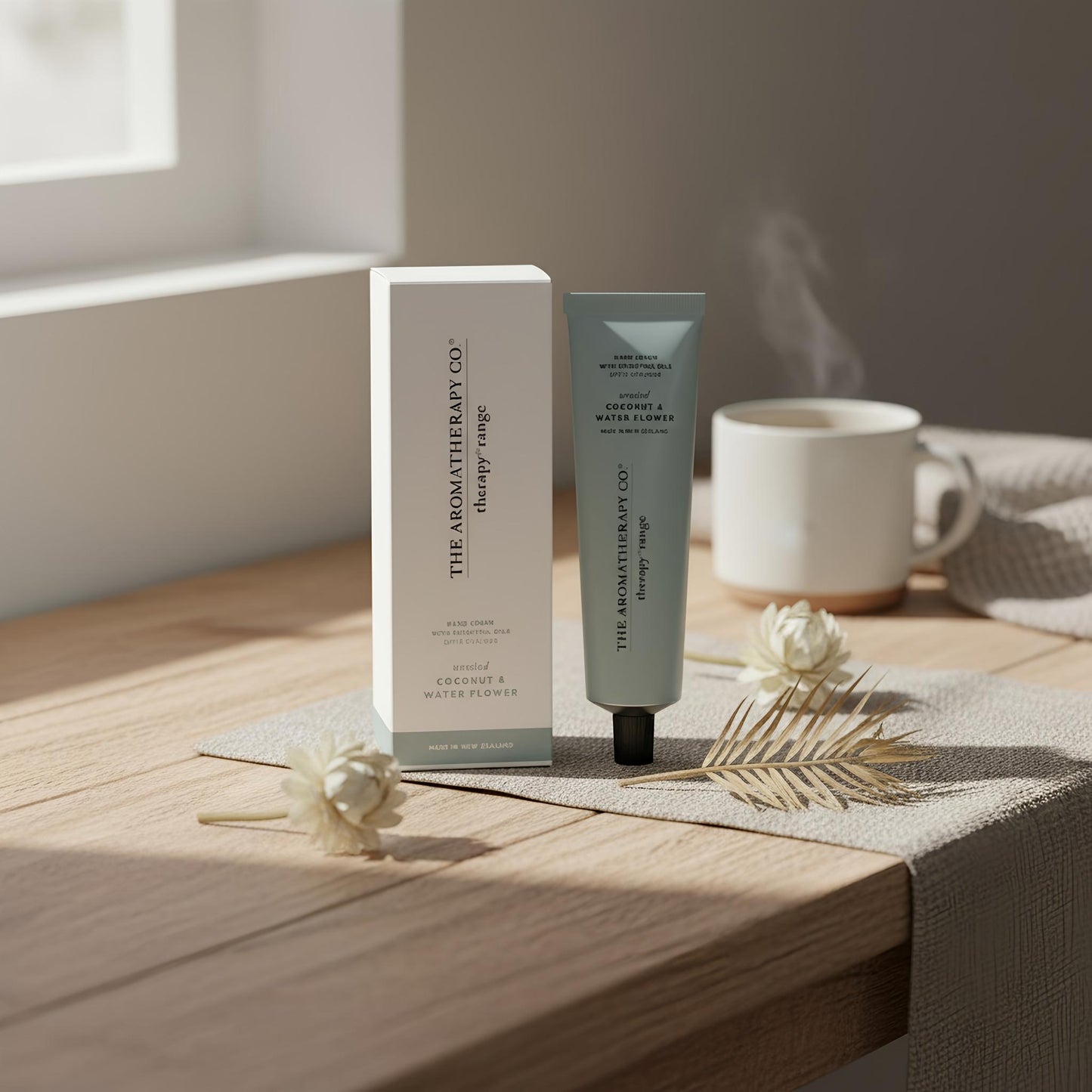 Cosmetic products from 'The Aromatherapy Co.' on a wooden surface with a cup of tea and flowers.