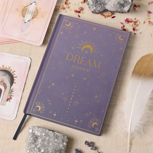 Purple 'Dream Journal' with celestial designs on a textured surface with cards and crystals.