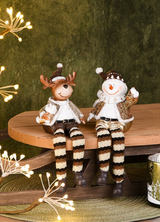 Two decorative figures of a reindeer and a snowman sitting on a wooden surface with a festive background.
