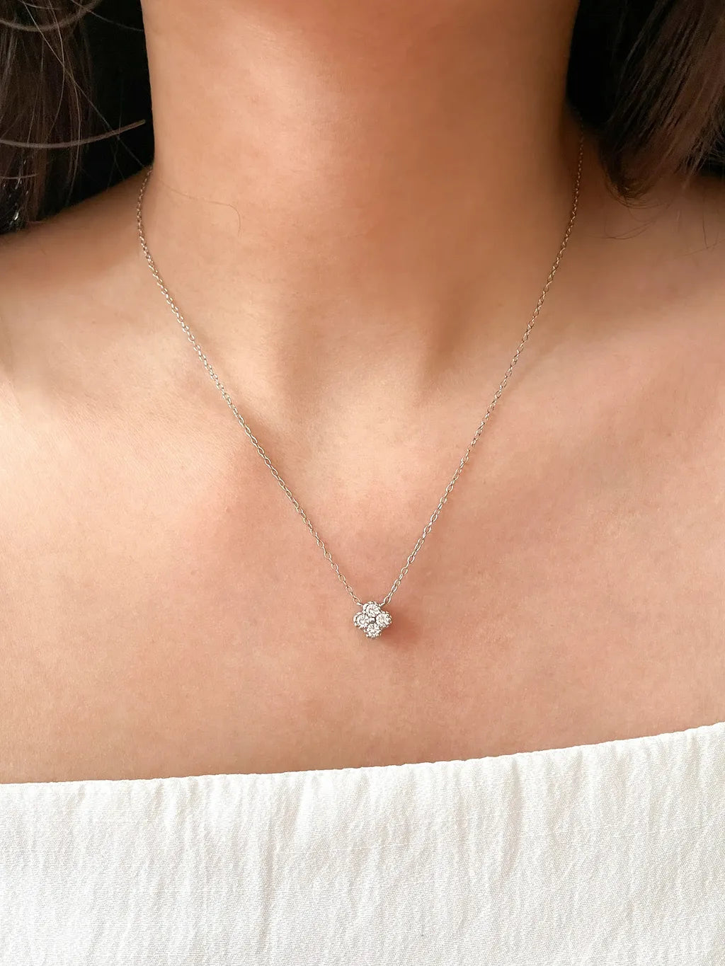 Silver necklace with a small pendant on a person wearing a white top.