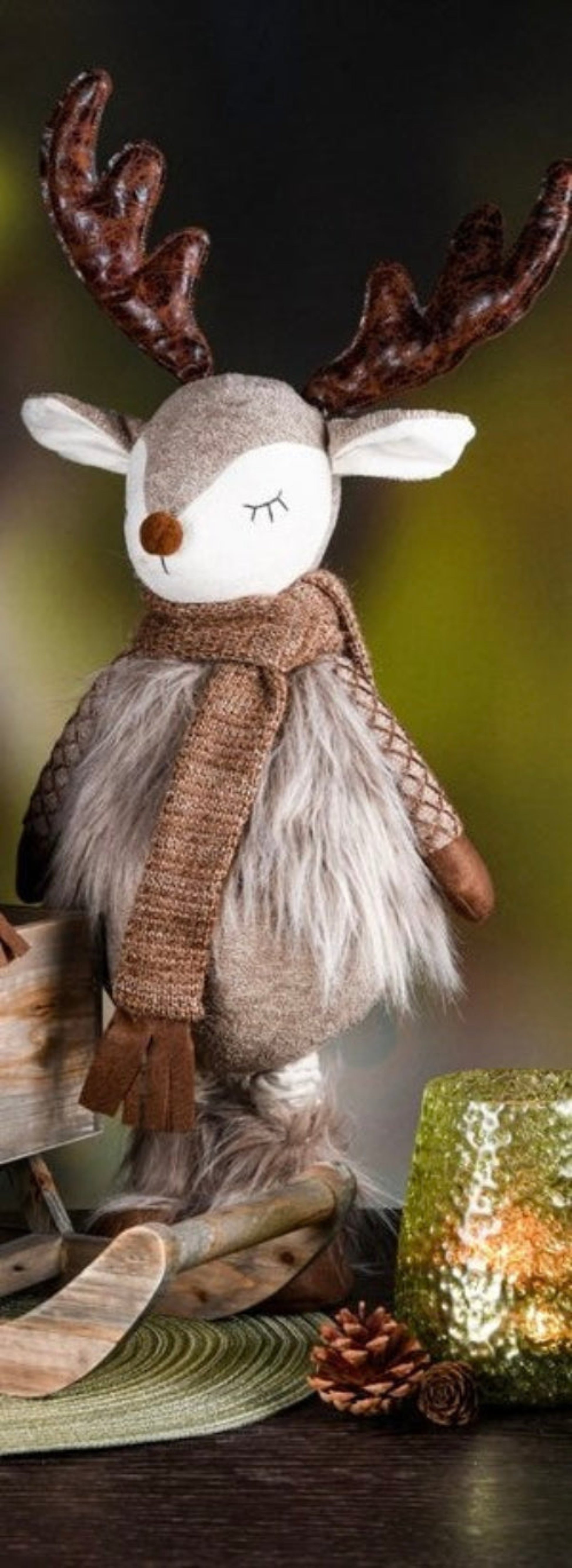 Stuffed reindeer with a scarf in a cozy setting with a candle and pinecones.